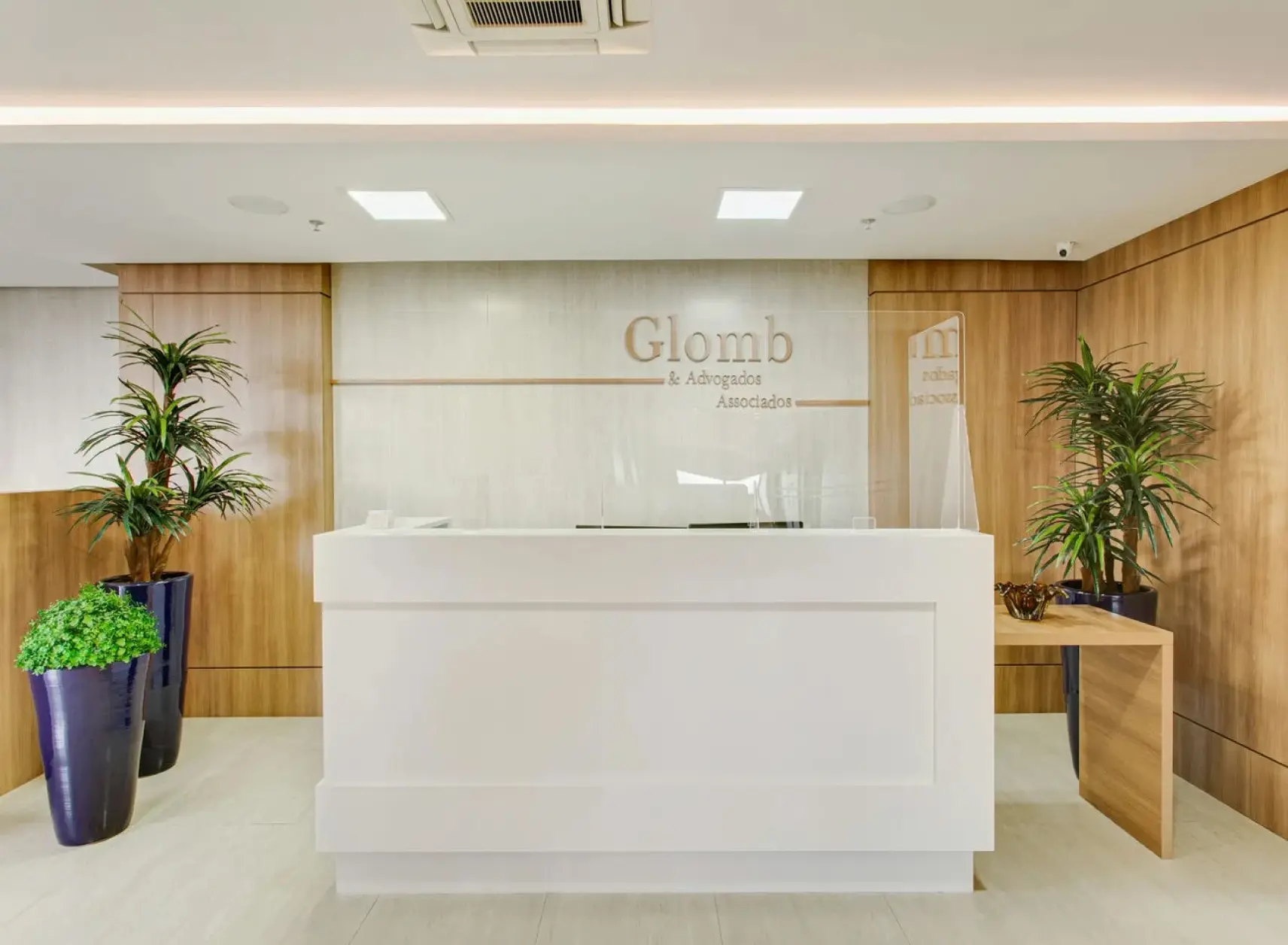 Entrada do escritório de advocacia Glomb Advogados, maior especialista em direito do trabalho e direito previdenciário do Brasil. Balcão da recepção branco com uma parede de mármore atrás e a logo do escritório.